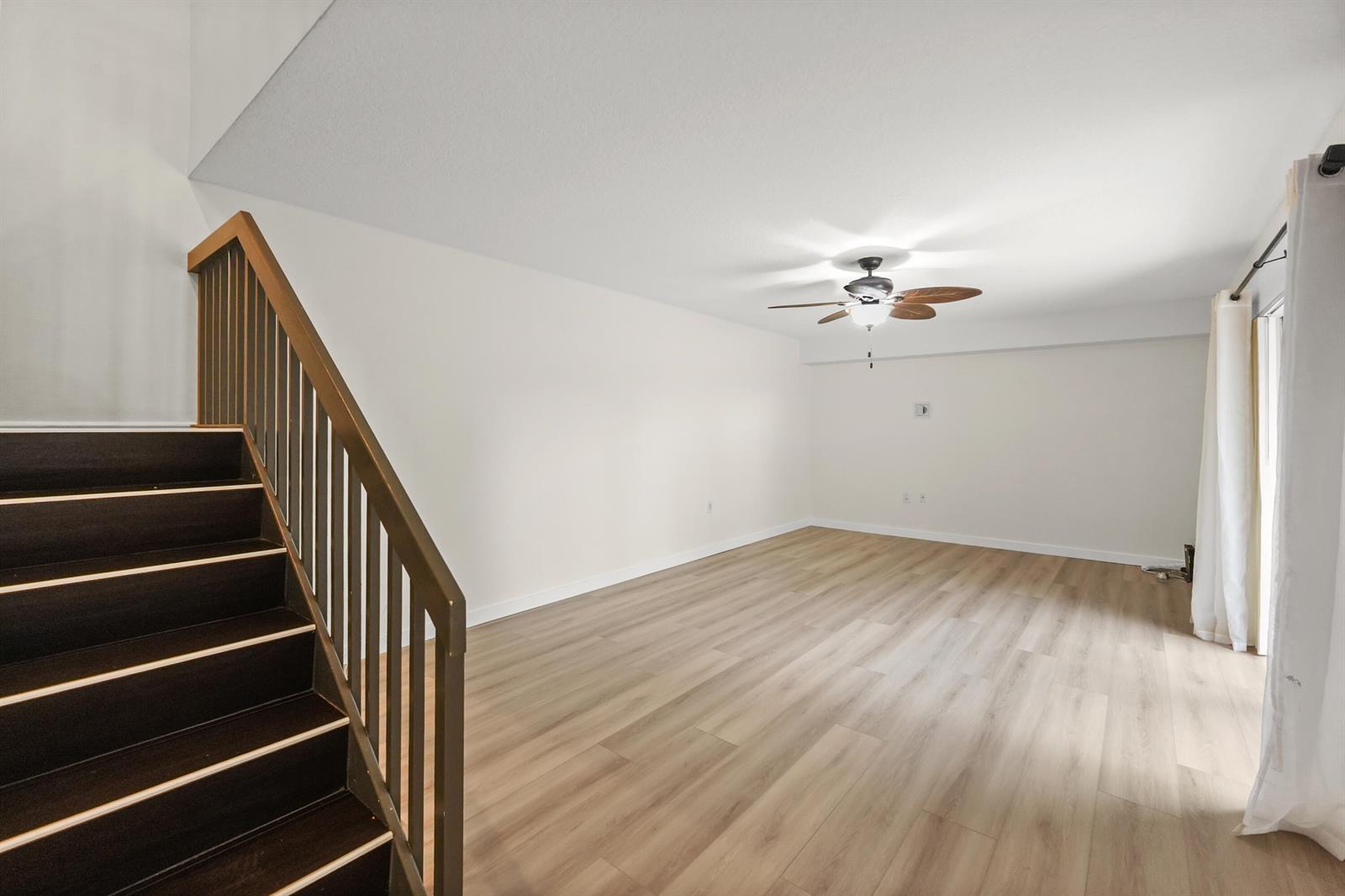 An empty living room with light wood-look flooring, a ceiling fan, and a wooden staircase — 6906 69th Way, West Palm Beach FL 33407, WEST PALM BEACH, FL