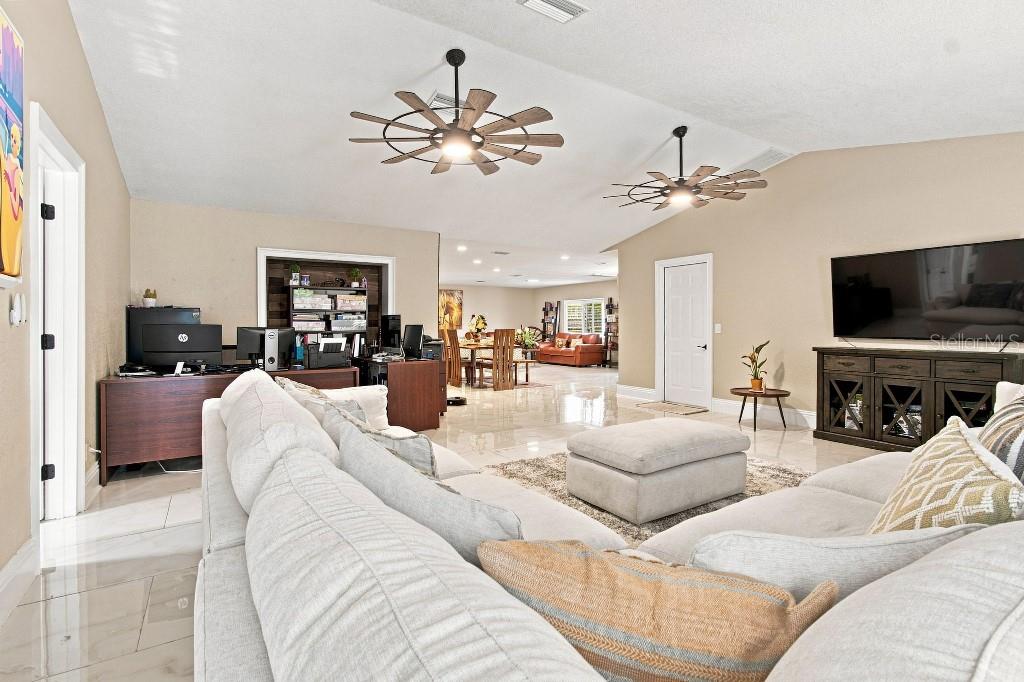 A spacious living room features two wagon-wheel ceiling fans, light tile flooring, and neutral walls — 17933 EAGLE LANE, LUTZ, FL