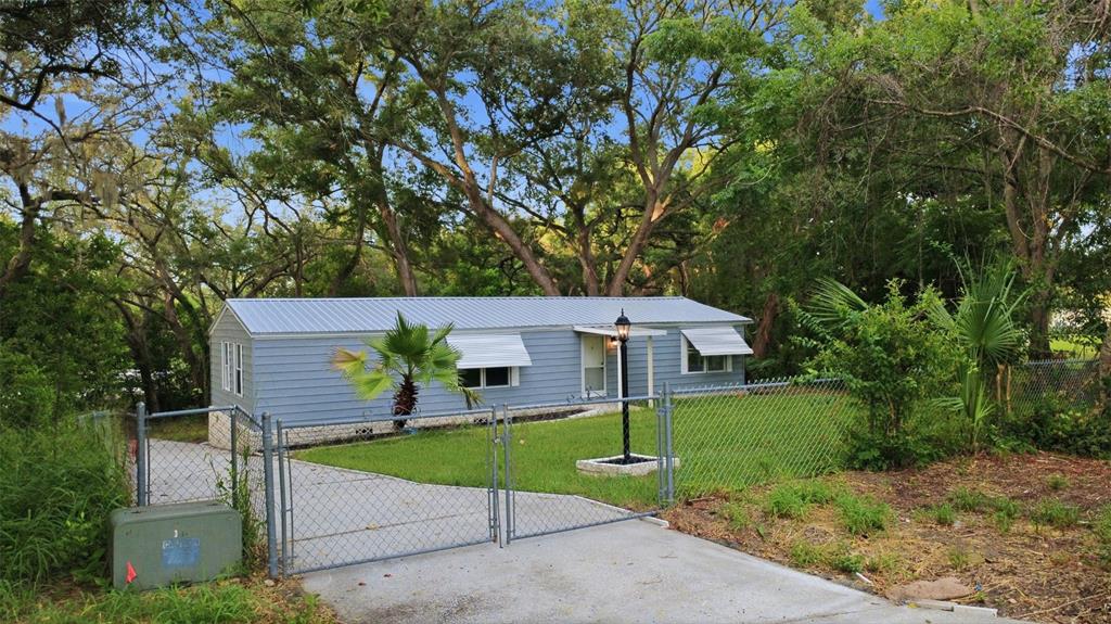 A light blue mobile home with a metal roof sits behind a chain-link fence — 403 ACORN CIRCLE, FRUITLAND PARK, FL