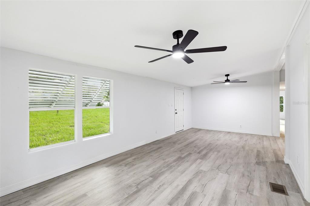 An empty room with white walls, light wood-look flooring, two ceiling fans, and two windows — 403 ACORN CIRCLE, FRUITLAND PARK, FL