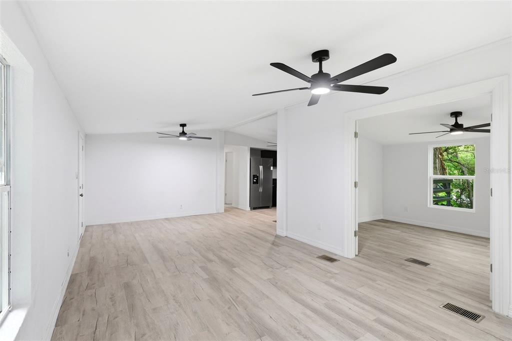 A bright, open-concept living area features light wood-look flooring, white walls, and ceiling fans — 403 ACORN CIRCLE, FRUITLAND PARK, FL