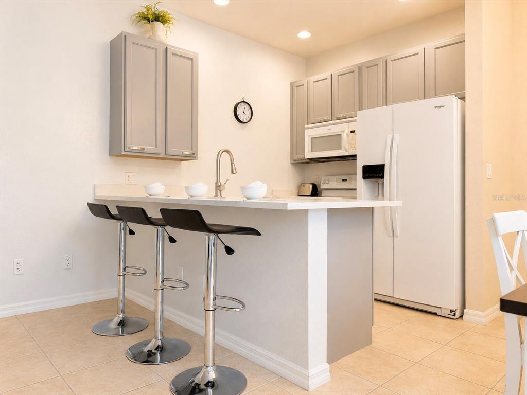 A kitchen features gray cabinets, a white refrigerator, and a breakfast bar with three stools — 2379 CARAVELLE CIRCLE, KISSIMMEE, FL