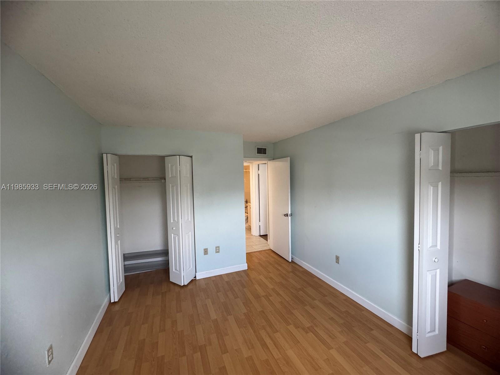 A bedroom with light blue walls, wood-look flooring, two closets, and an open doorway — 8075 NW 7th St # 403, Miami FL 33126, MIAMI, FL