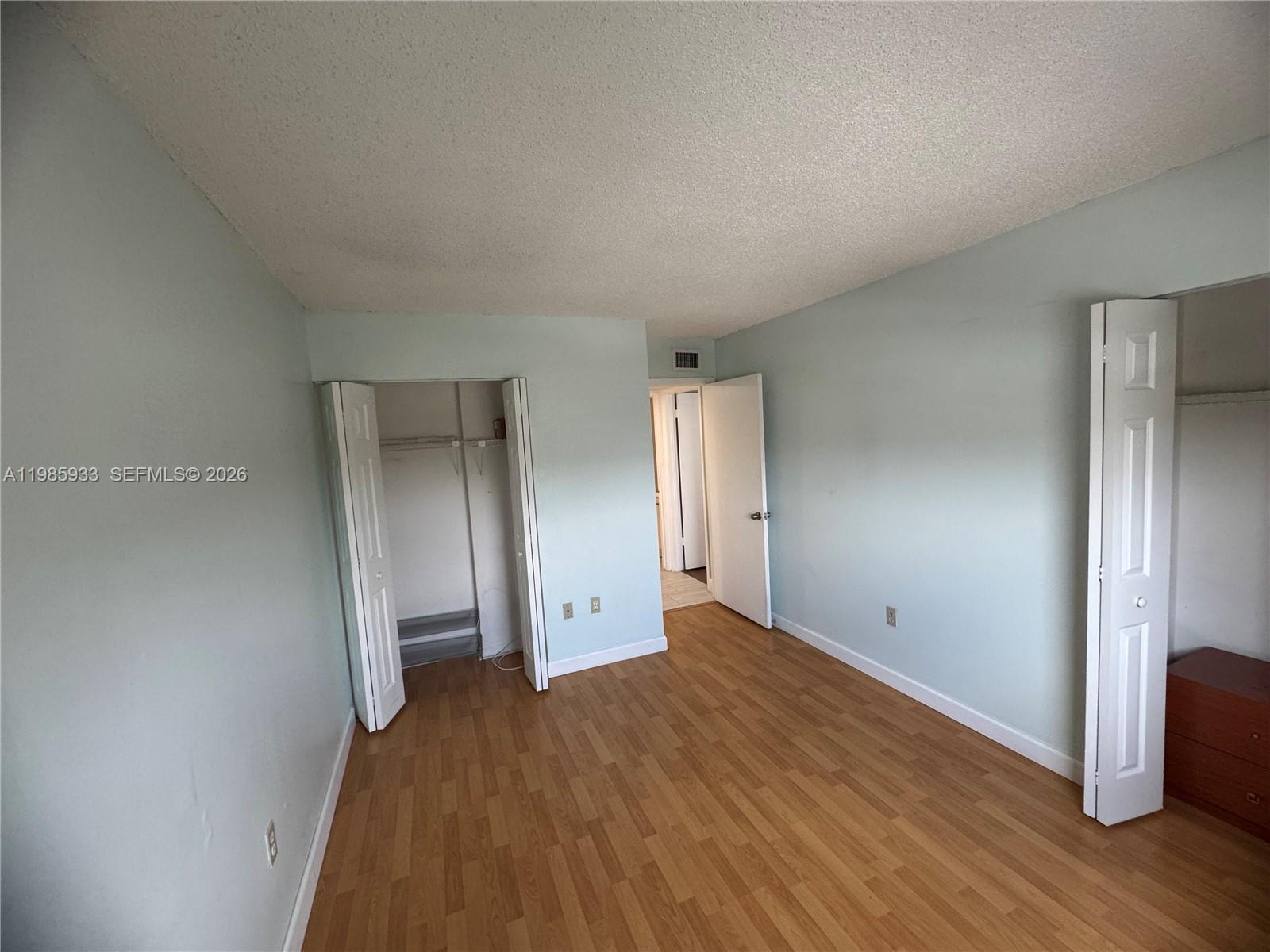 An empty bedroom features light blue walls, wood-look flooring, and two open closets — 8075 NW 7th St # 403, Miami FL 33126, MIAMI, FL