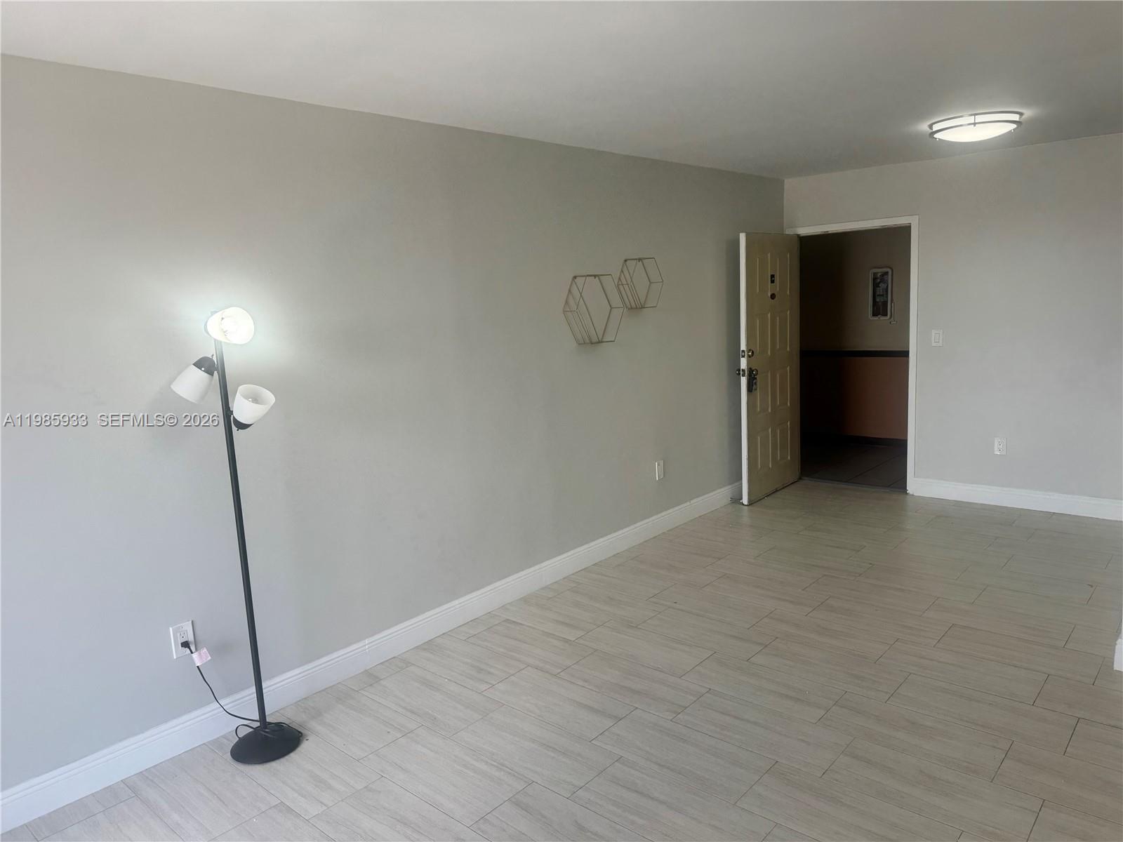 A room with light gray walls, wood-look tile flooring, a floor lamp, and an open doorway — 8075 NW 7th St # 403, Miami FL 33126, MIAMI, FL