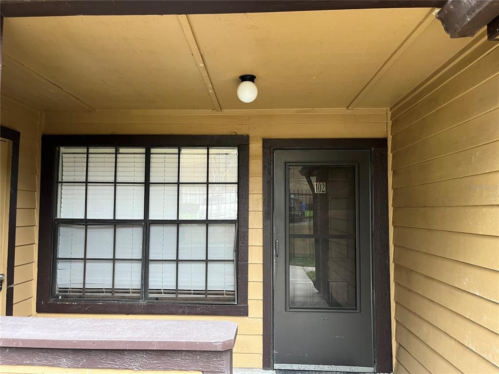A yellow-sided building exterior features a window with white blinds and a door labeled 102 — 355 LAKEPOINTE DRIVE UNIT 102, ALTAMONTE SPRINGS, FL