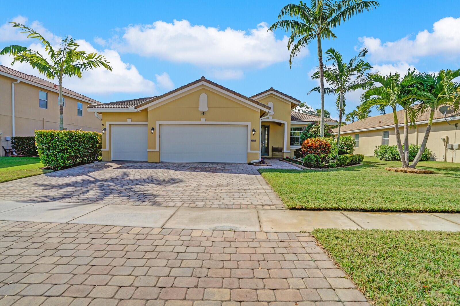 A yellow single-story house features a paver driveway, a three-car garage, and palm trees — 9328 Silent Oak Circle, West Palm Beach FL 33411, WEST PALM BEACH, FL