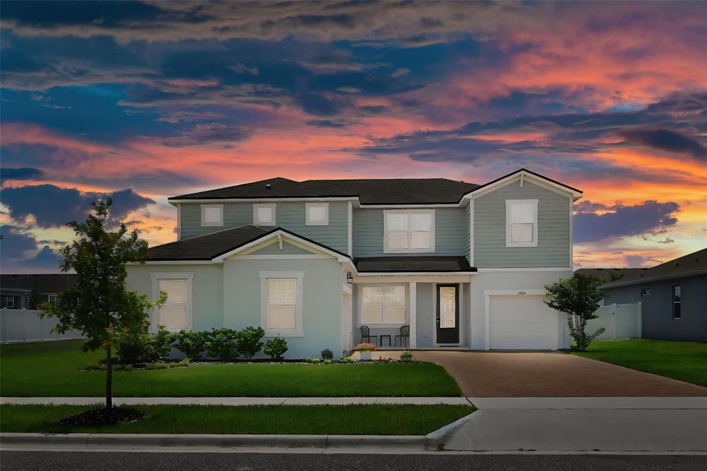 A two-story house with light green siding, a dark roof, and a paved driveway at sunset — 2666 GINSENG IVY STREET, APOPKA, FL