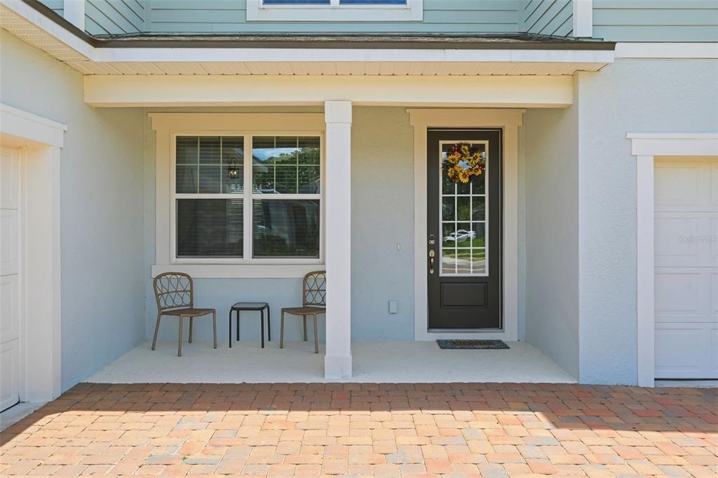 A covered porch features a brick paver floor, two chairs, a small table, and a door — 2666 GINSENG IVY STREET, APOPKA, FL