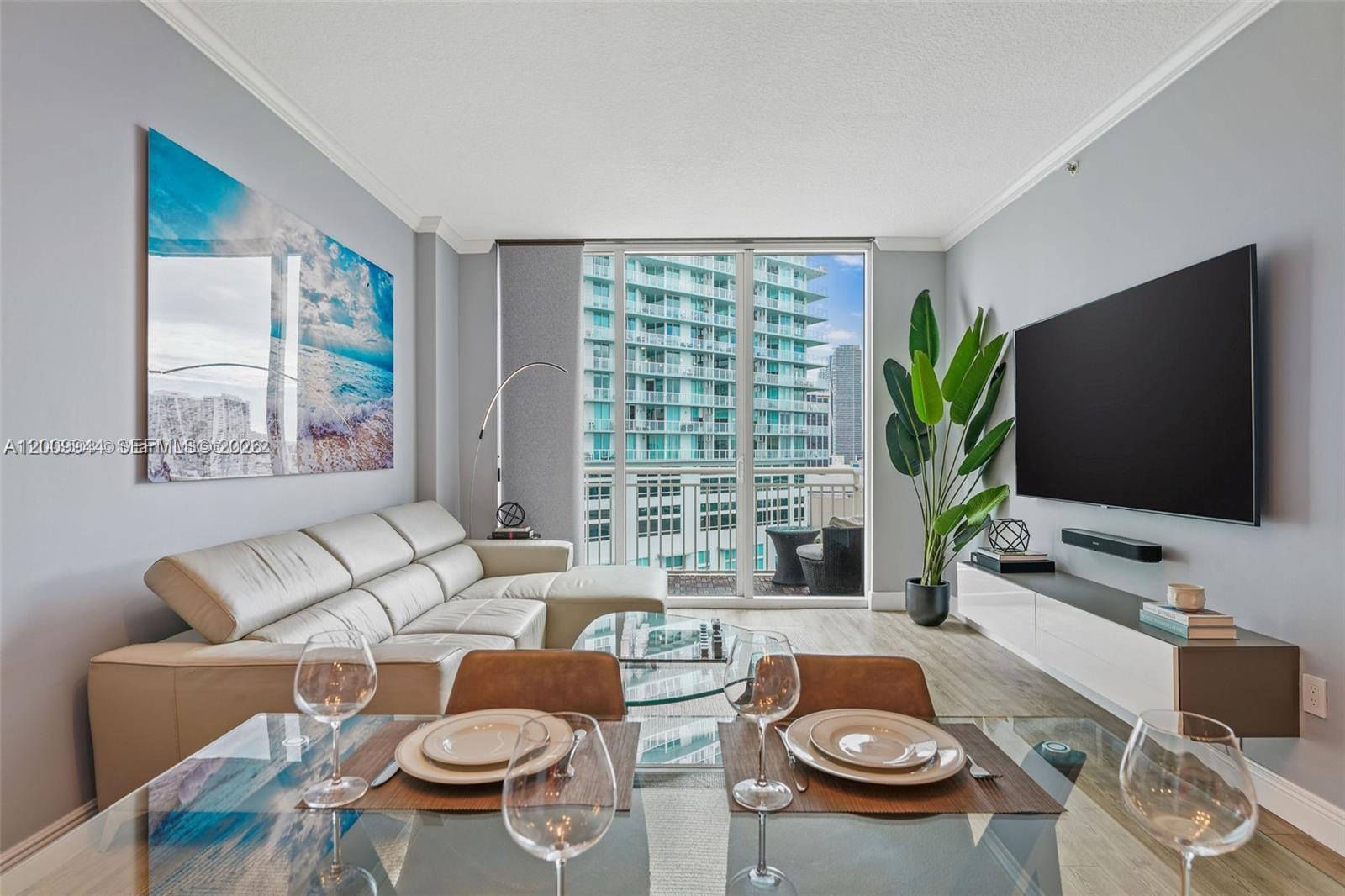 A modern living and dining area features a white sectional sofa, glass table, and balcony — 2000 N Bayshore Dr # 1606, Miami FL 33137, MIAMI, FL