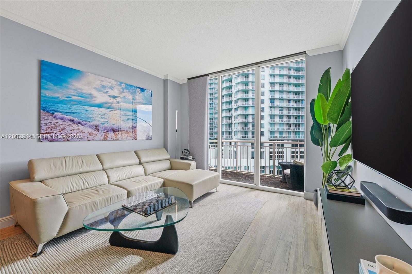 A modern living room features a beige sectional sofa, glass coffee table, and balcony view — 2000 N Bayshore Dr # 1606, Miami FL 33137, MIAMI, FL