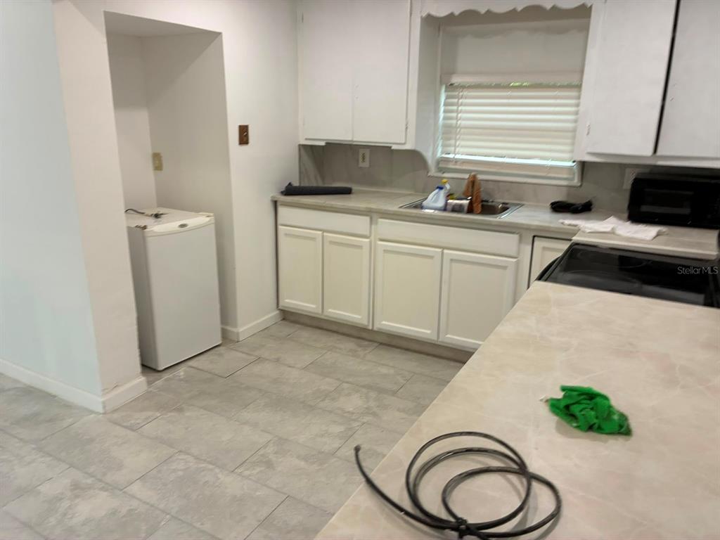 A kitchen features white cabinets, a stainless steel sink, and light-colored tile flooring — 106 PENNSYLVANIA AVENUE, POMONA PARK, FL