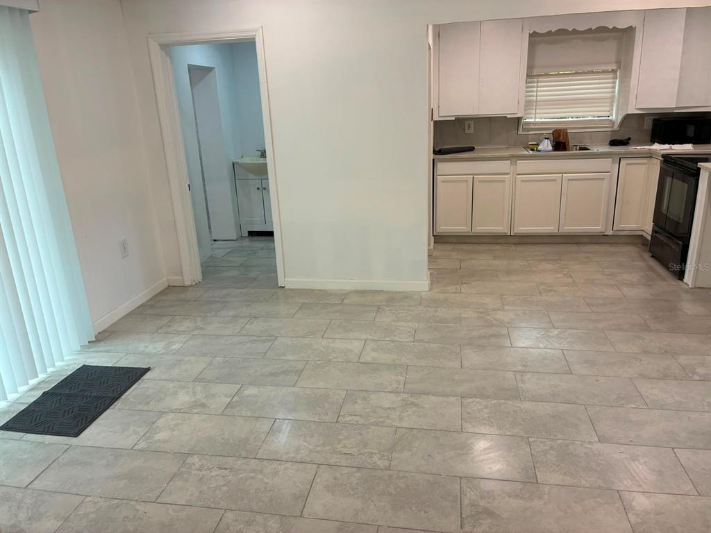 A kitchen with white cabinets and gray tile flooring opens to a hallway and bathroom — 106 PENNSYLVANIA AVENUE, POMONA PARK, FL