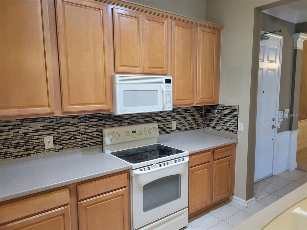 A kitchen features light wood cabinets, a white stove, a microwave, and a mosaic backsplash — 7905 N SEMINOLE BOULEVARD UNIT 3404, SEMINOLE, FL