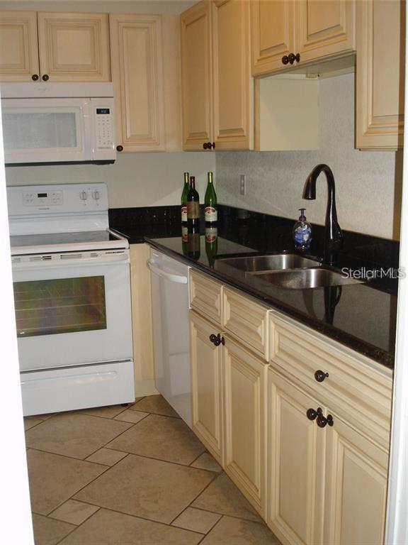 A kitchen features cream-colored cabinets, black countertops, white appliances, and a double-basin sink — 7211 W COUNTRY CLUB DRIVE N UNIT 133, SARASOTA, FL