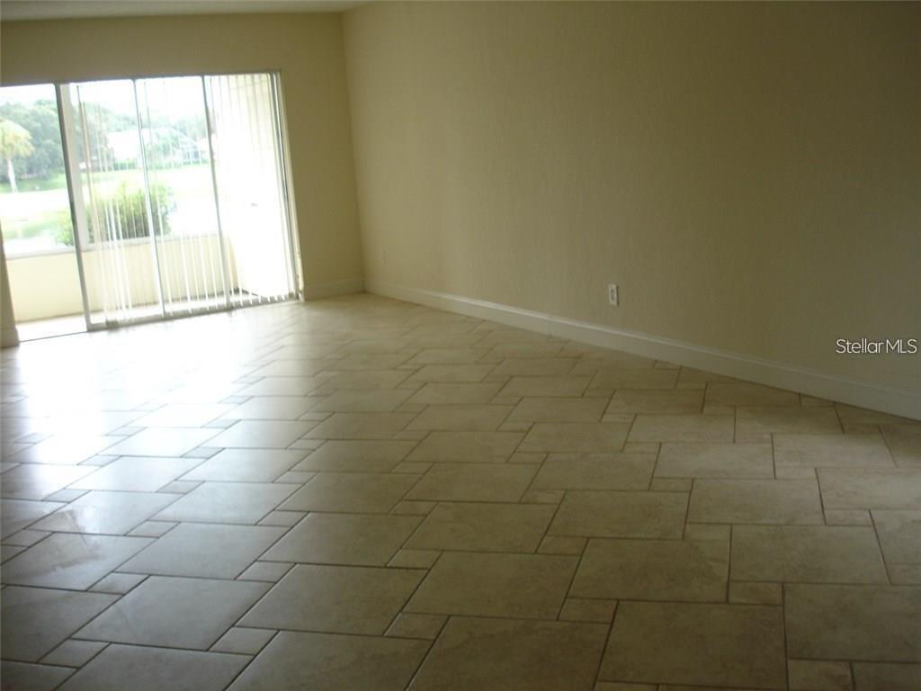 An empty room features beige tile flooring and a sliding glass door leading to a balcony — 7211 W COUNTRY CLUB DRIVE N UNIT 133, SARASOTA, FL