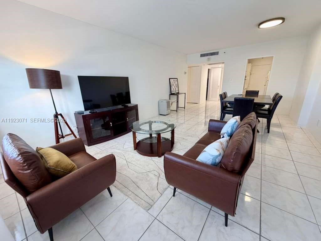 This living and dining area features white tile floors, brown leather furniture, and a television — 100 Lincoln Rd # 541, Miami Beach FL 33139, MIAMI BEACH, FL