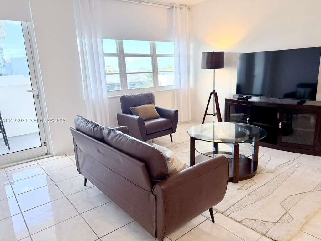 A living room features white tile floors, a brown sofa, an armchair, and a television — 100 Lincoln Rd # 541, Miami Beach FL 33139, MIAMI BEACH, FL