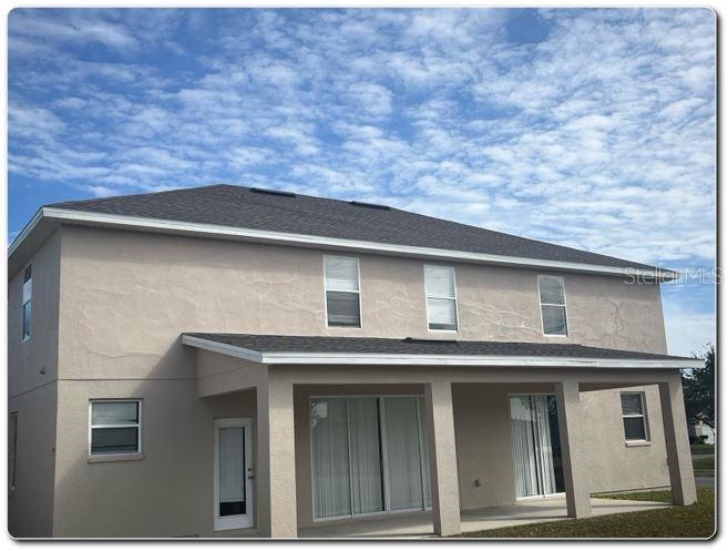 The rear exterior of a two-story beige stucco house features a covered patio and roof — 2887 SWEETSPIRE CIRCLE, KISSIMMEE, FL