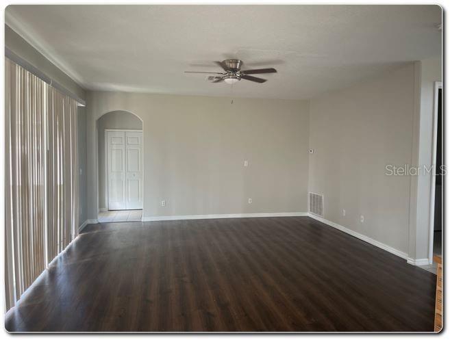 An empty living room with dark wood-look flooring, light walls, and a ceiling fan — 2887 SWEETSPIRE CIRCLE, KISSIMMEE, FL