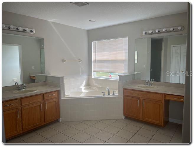 A bathroom features two wooden vanities with mirrors and a central soaking tub under a window — 2887 SWEETSPIRE CIRCLE, KISSIMMEE, FL