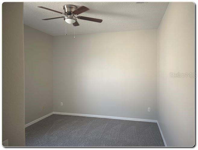 An empty room features beige walls, gray carpeting, and a ceiling fan — 2887 SWEETSPIRE CIRCLE, KISSIMMEE, FL