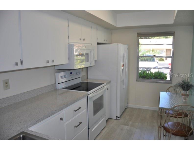 A kitchen features white cabinets, white appliances, a speckled countertop, and a small dining area — 2630 WOODGATE LANE UNIT G3, SARASOTA, FL