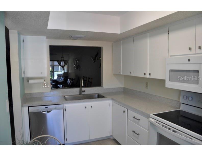 A kitchen with white cabinets, stainless steel appliances, and a pass-through window to the living area — 2630 WOODGATE LANE UNIT G3, SARASOTA, FL