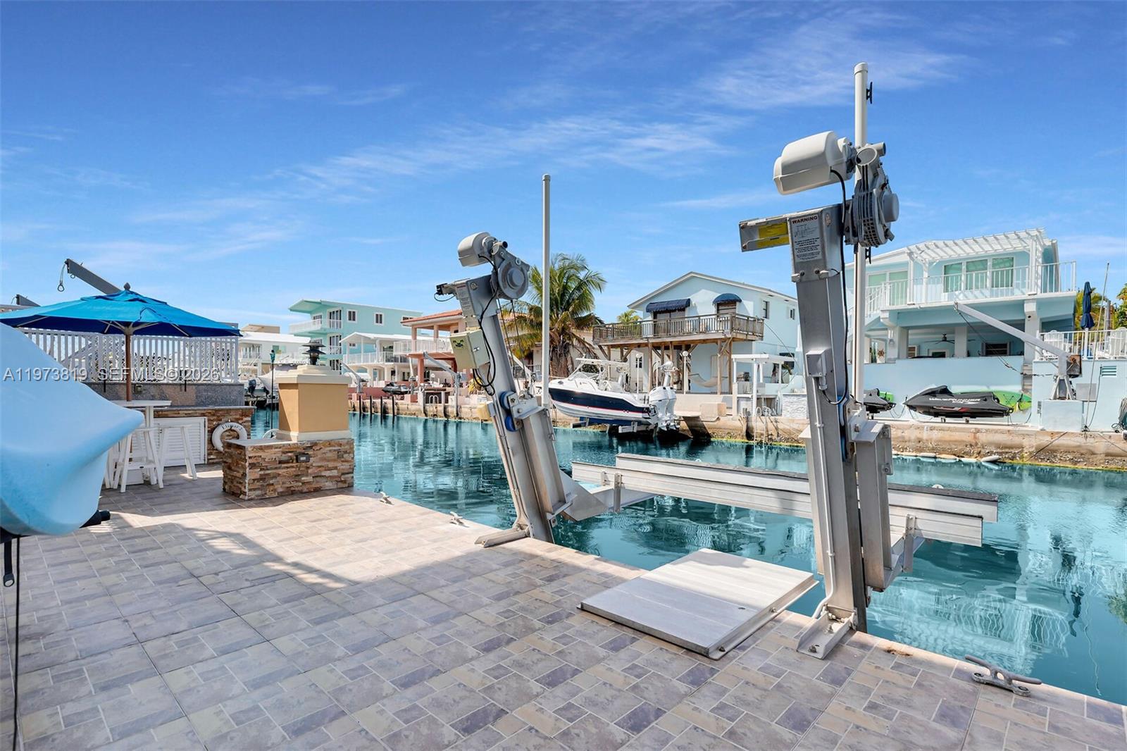 A tiled patio overlooks a canal featuring a boat lift and nearby waterfront homes — 226 Normandy Dr, Tavernier FL 33070, TAVERNIER, FL