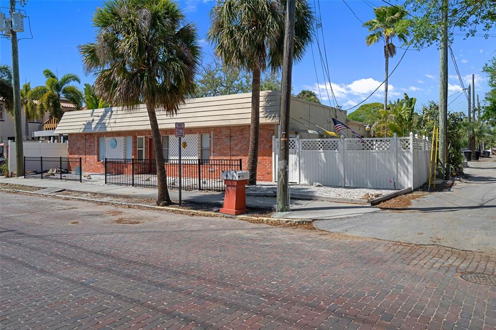 A single-story brick building with a white fence and palm trees on a brick street — 5437 29TH AVENUE S, GULFPORT, FL