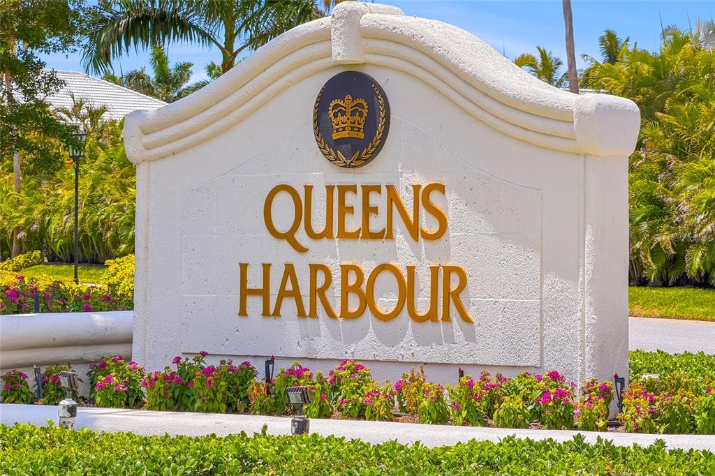 A white monument sign with gold lettering reads Queens Harbour under a crown emblem — 3526 FAIR OAKS LANE, LONGBOAT KEY, FL