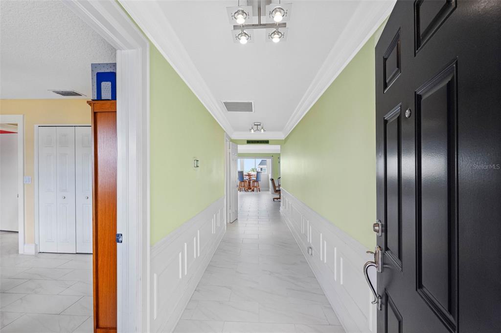 A hallway with light green walls, white wainscoting, and tile flooring leads toward a dining area — 139 BLUFF VIEW DRIVE UNIT 407, BELLEAIR BLUFFS, FL