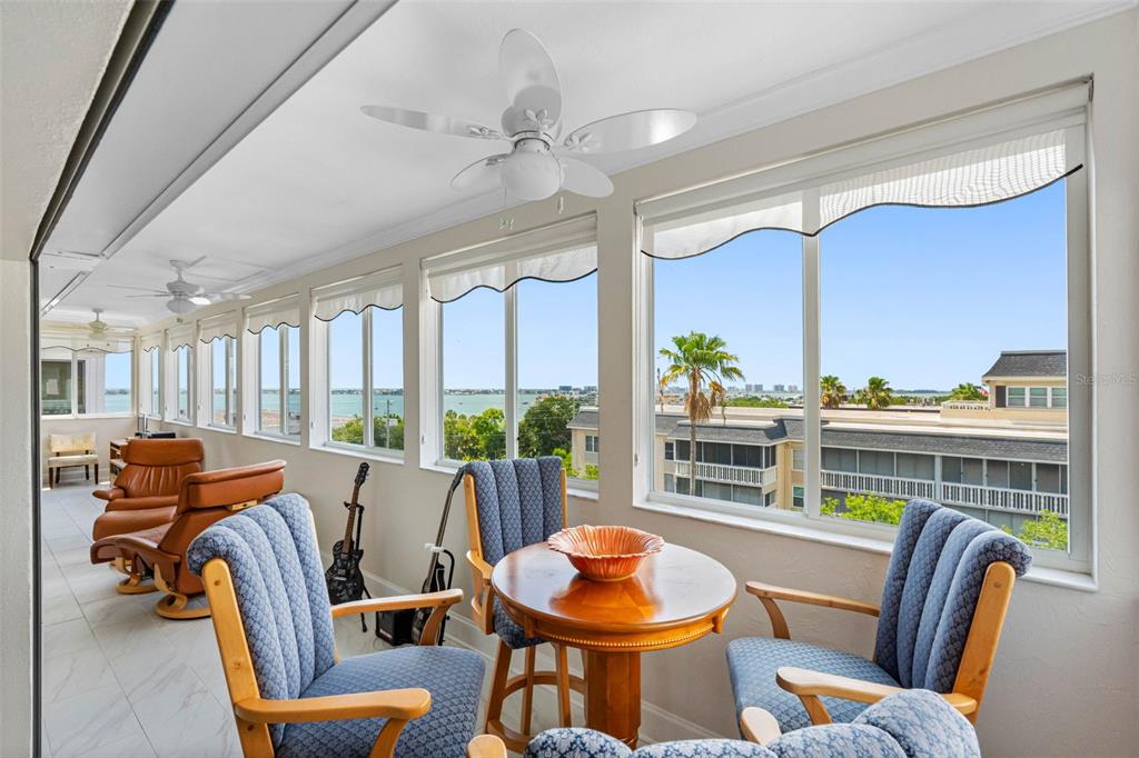A sunroom features blue upholstered chairs, a wooden table, and large windows overlooking the water — 139 BLUFF VIEW DRIVE UNIT 407, BELLEAIR BLUFFS, FL