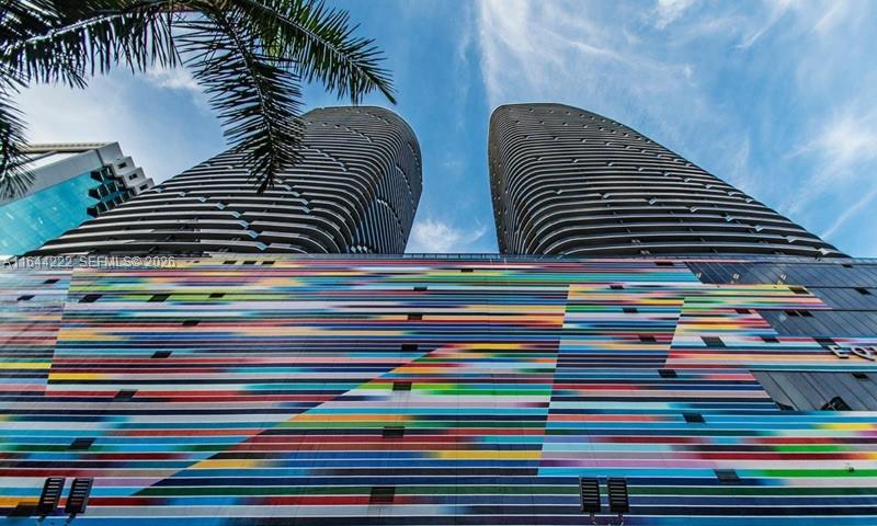 A low-angle exterior view of two modern high-rise towers featuring a colorful, horizontally striped mural — 45 SW 9th St # 1005, Miami FL 33130, MIAMI, FL