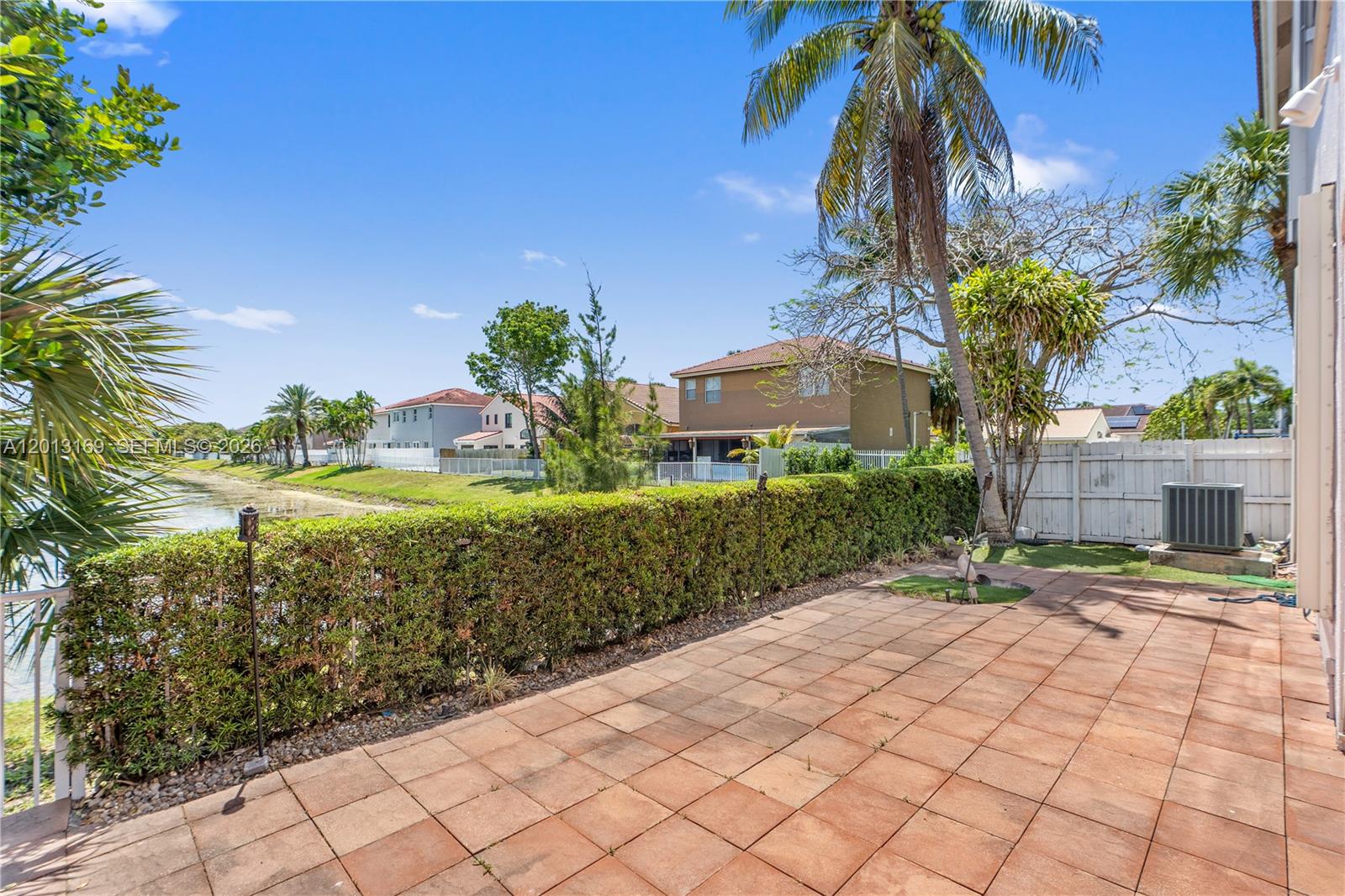 A tiled patio overlooks a grassy yard, a hedge, and a small pond — 3760 SW 51st St, Hollywood FL 33312, HOLLYWOOD, FL