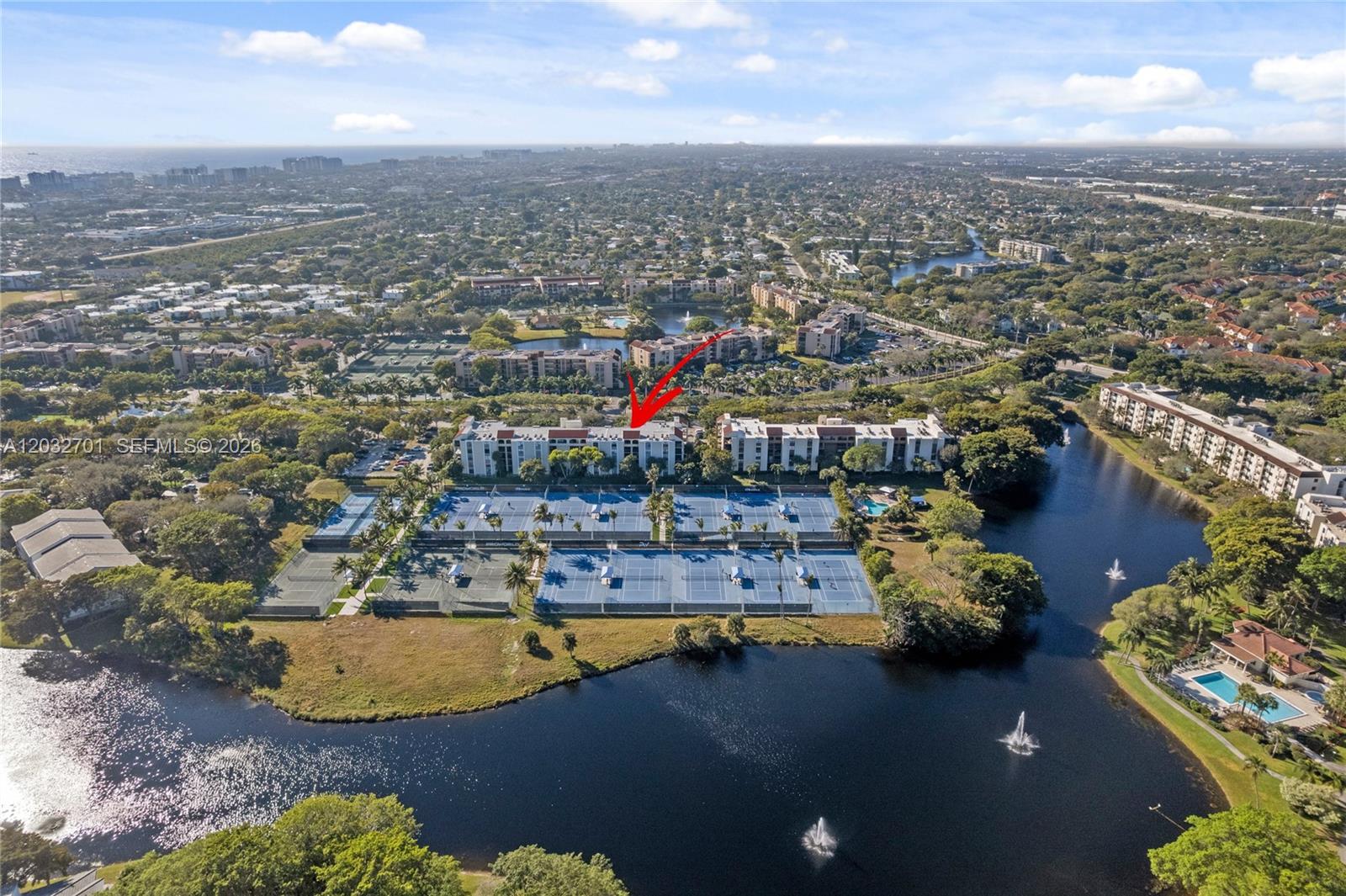 An aerial view shows a residential building complex surrounded by tennis courts and a lake — 825 Egret Cir # 504, Delray Beach FL 33444, DELRAY BEACH, FL