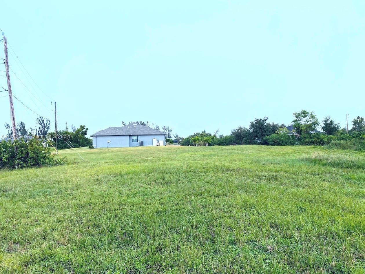 A large, grassy vacant lot sits in front of a single-story blue house — 809 NW 29th Ave, Cape Coral FL 33993, CAPE CORAL, FL