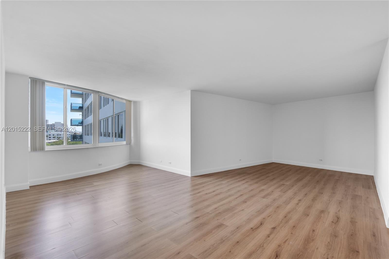 An empty room features white walls, light wood-look flooring, and a large corner window — 7441 Wayne Ave # 4G, Miami Beach FL 33141, MIAMI BEACH, FL