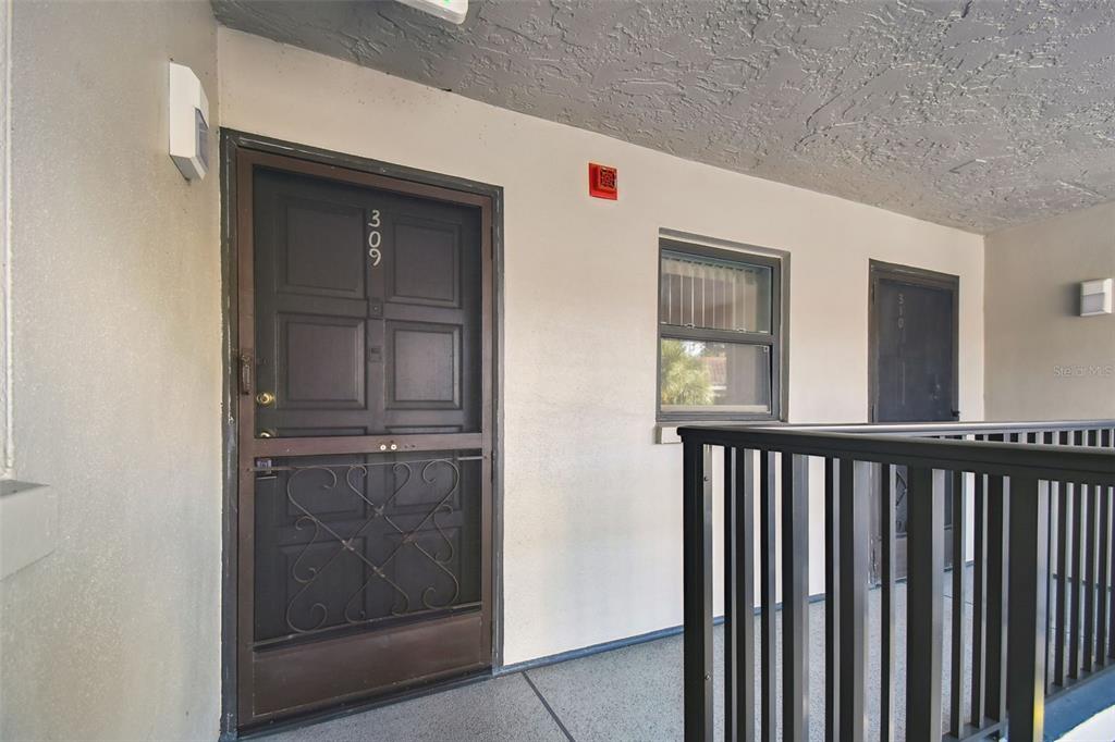 An exterior hallway shows two apartment doors with screen doors and a window between them — 2650 COUNTRYSIDE BOULEVARD UNIT C309, CLEARWATER, FL