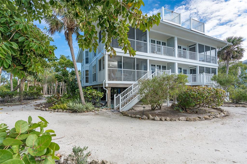 A three-story, light blue coastal home features screened-in porches, white railings, and a sandy yard — 7536 PALM ISLAND DRIVE S UNIT 1522, PLACIDA, FL