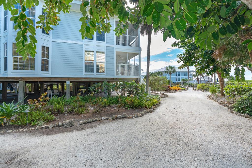 A light blue stilt house with a gravel path and lush landscaping in the foreground — 7536 PALM ISLAND DRIVE S UNIT 1522, PLACIDA, FL