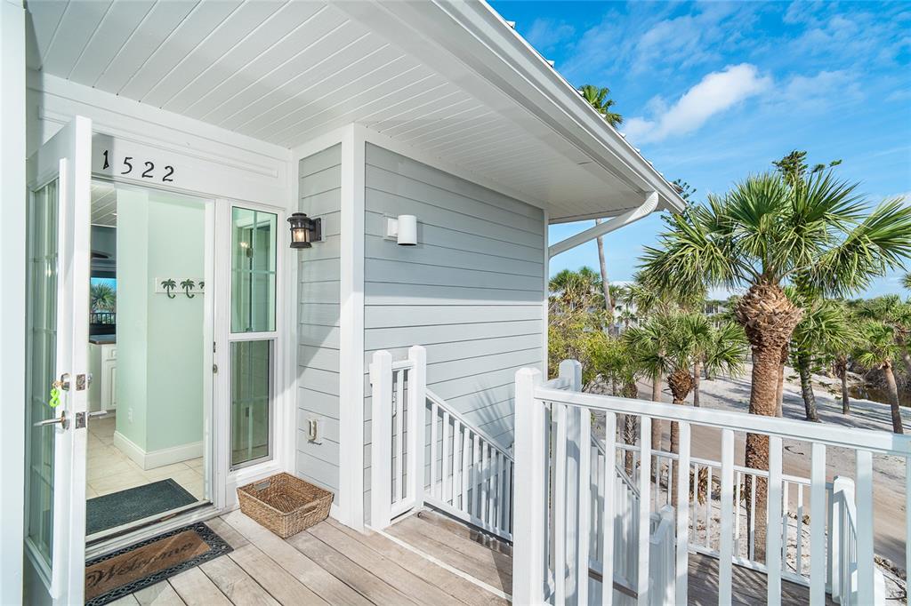 An elevated wooden deck leads to an open doorway of a light blue coastal home — 7536 PALM ISLAND DRIVE S UNIT 1522, PLACIDA, FL