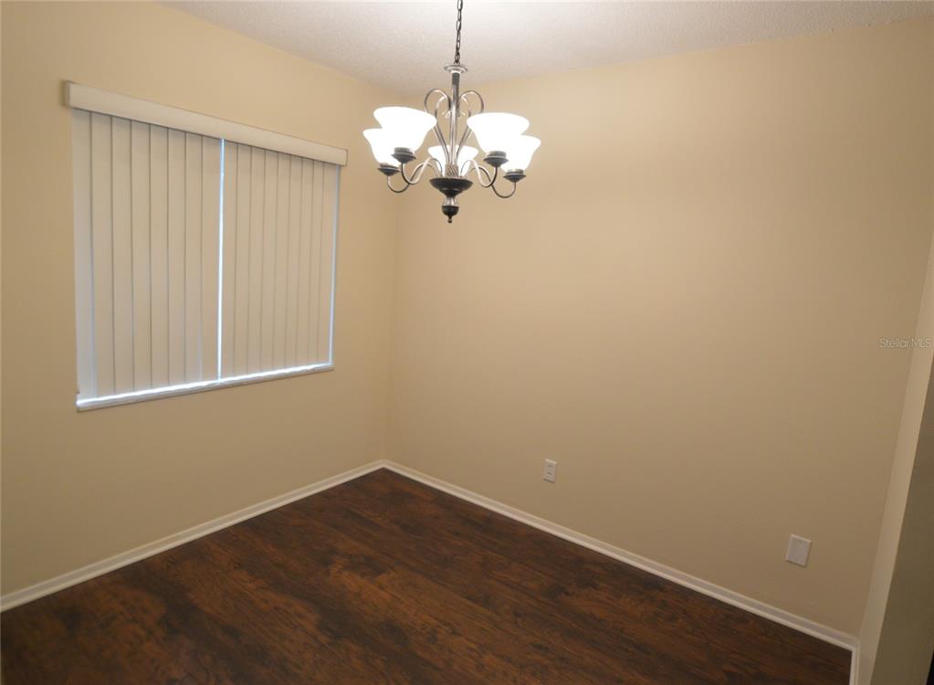 An empty dining room features dark wood-look flooring, beige walls, and a hanging chandelier — 7509 PRESLEY PLACE UNIT 96, TAMPA, FL