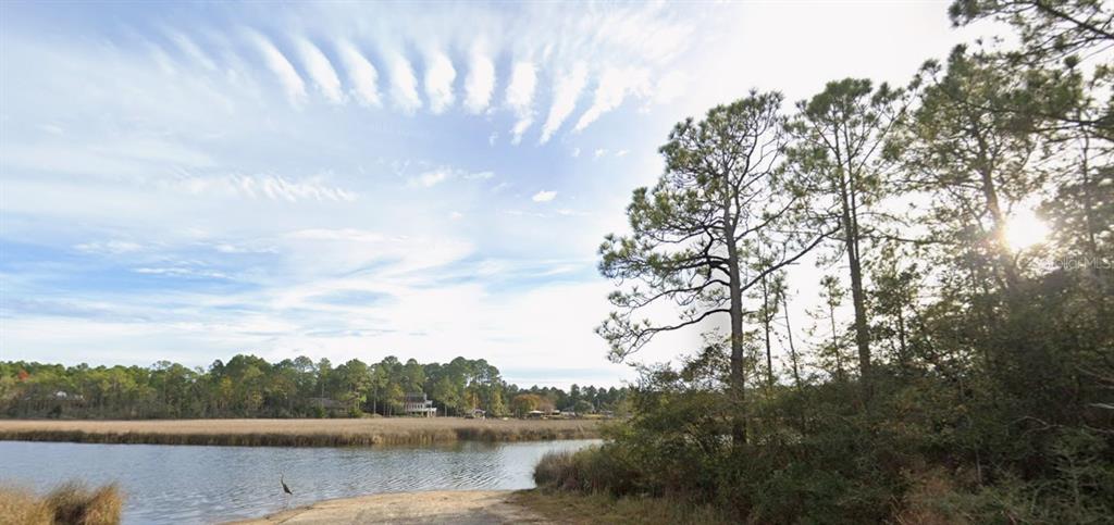 A view of a calm river with a grassy bank and trees under a cloudy sky — 5599 DEL REY STREET, MILTON, FL