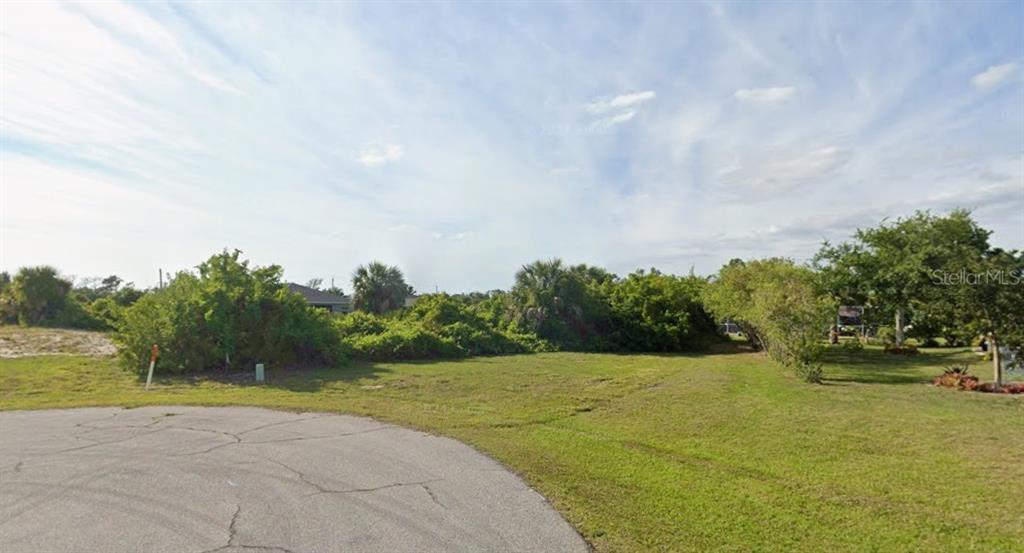 A vacant, grassy residential lot with dense vegetation and trees under a blue sky — 108 GREEN OAK PARK, ROTONDA WEST, FL