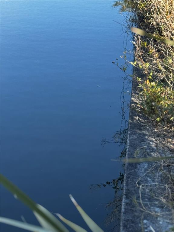 A concrete edge borders a calm, dark blue body of water with nearby vegetation — 1715 NE 13TH TERRACE, CAPE CORAL, FL