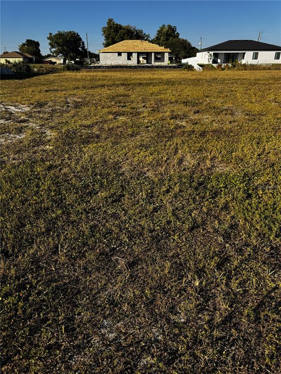 A vacant, grassy lot sits in front of a house under construction and a finished home — 1715 NE 13TH TERRACE, CAPE CORAL, FL