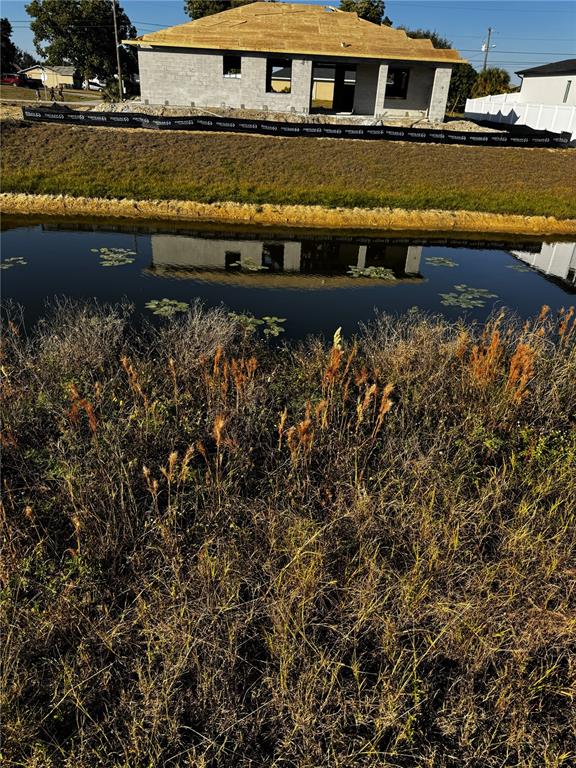 A house under construction sits behind a small pond and a field of tall grass — 1715 NE 13TH TERRACE, CAPE CORAL, FL