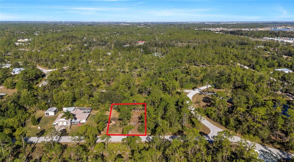An aerial view shows a vacant, rectangular lot outlined in red within a wooded neighborhood — 28118 INCHON AVENUE, PUNTA GORDA, FL