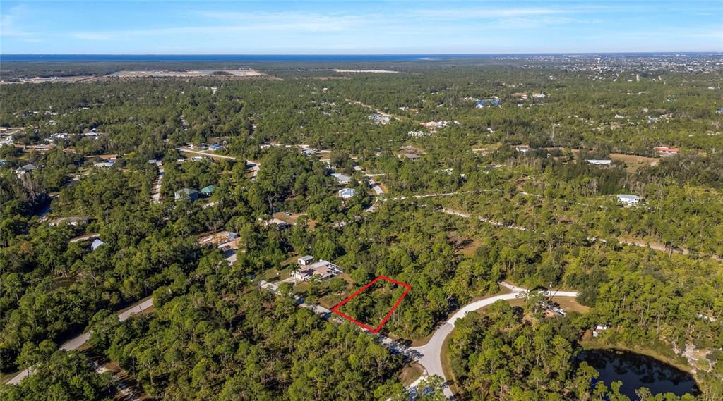 An aerial view shows a vacant, rectangular lot outlined in red within a wooded neighborhood — 28118 INCHON AVENUE, PUNTA GORDA, FL